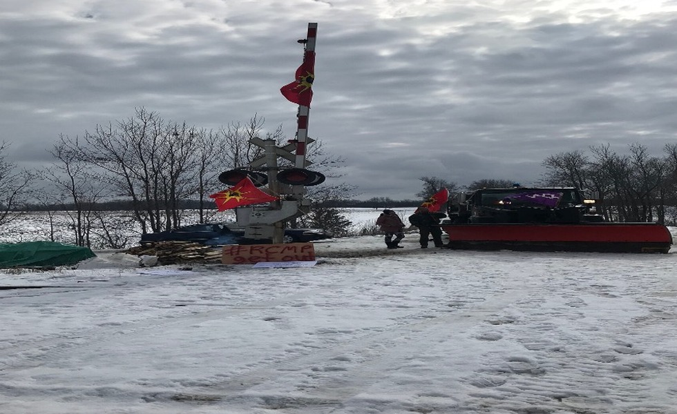 Une structure en forme de canot et un drapeau mohawk occupent le passage à niveau enneigé pendant le blocus ferroviaire de Tyendinaga. Photo : Bobby-Jo Morris / Wikimedia Commons.