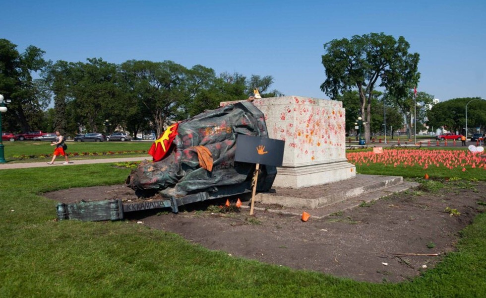 La statue de la reine Victoria gît renversée devant l’Assemblée législative du Manitoba, recouverte de peinture orange et rouge. Photo : Reuters / Getty Images.