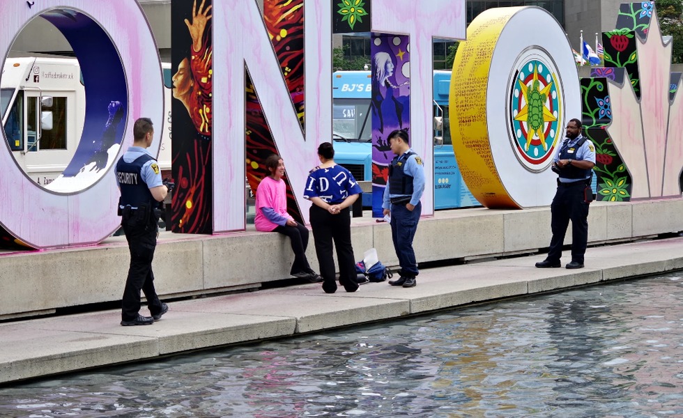 Le panneau Toronto est taché de peinture rose; des policiers et des témoins entourent le bassin réfléchissant après l’action du 8 août 2023. Photo : On2Ottawa / médias sociaux.