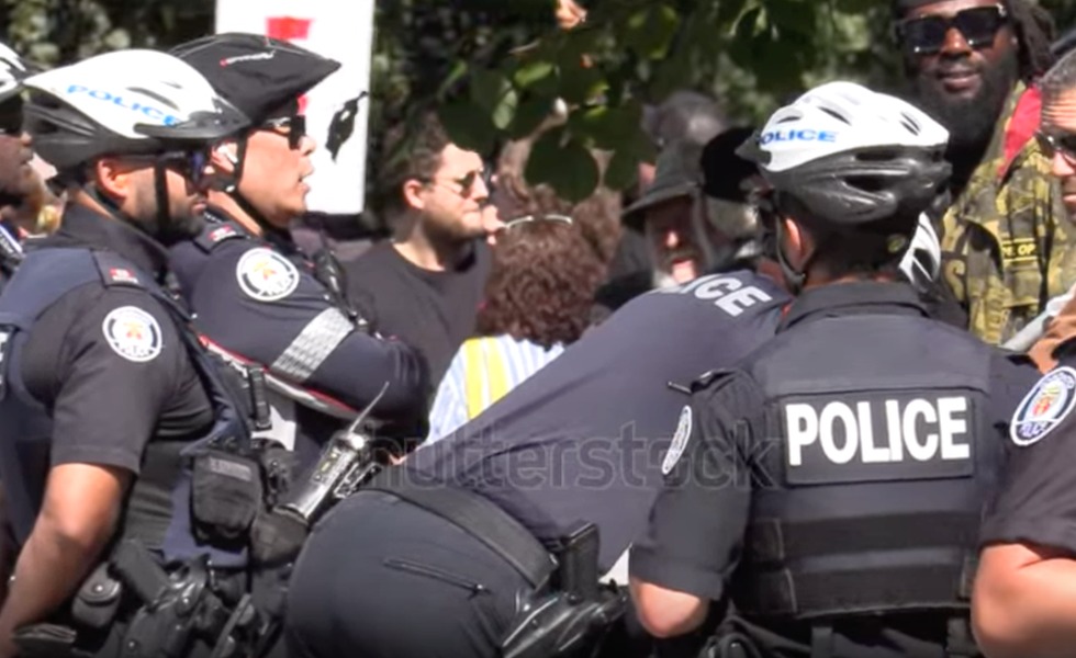 Nicholas Alexander, le visage ensanglanté, se tient au milieu de policiers de Toronto après une altercation à Queen’s Park. Photo : Rebel News / Save Canada.