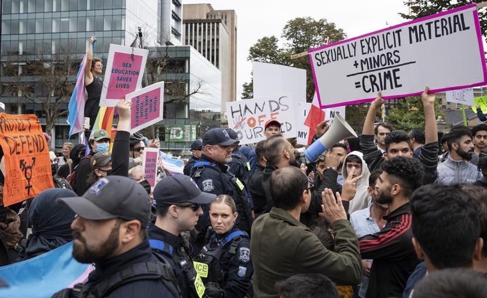 Une importante foule de manifestants et de contre-manifestants est séparée par des policiers; des pancartes dénonçant du matériel sexuellement explicite sont visibles. Photo : Sean Kilpatrick / La Presse canadienne, publiée par CityNews.