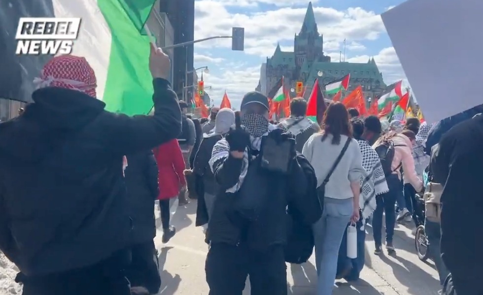 Des manifestants portant des keffiehs et des drapeaux palestiniens défilent sur la Colline du Parlement pendant la Marche nationale pour la Palestine. Capture du reportage de Rebel News.