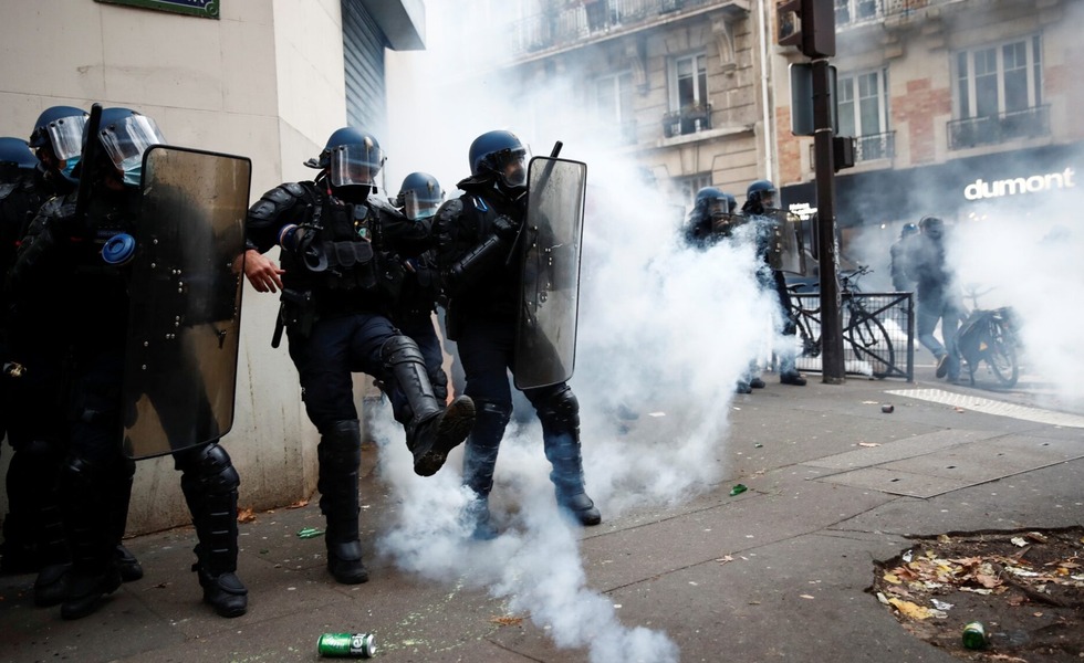 Des policiers antiémeute courent dans une rue de Paris envahie par les gaz lacrymogènes, au milieu de débris laissés après les affrontements du 28 novembre 2020.