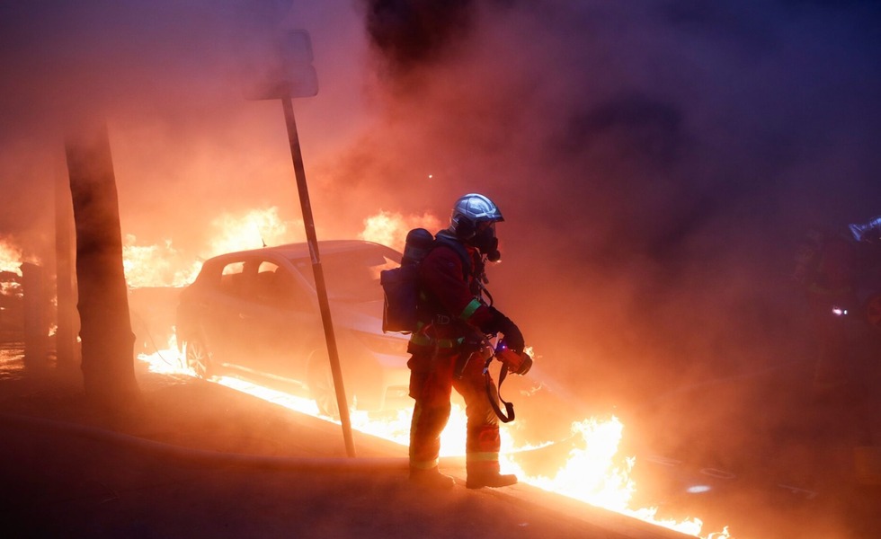 Un policier antiémeute se tient près d’un véhicule et de barricades en flammes, dans une rue de Paris noyée par la fumée le 5 décembre 2020.