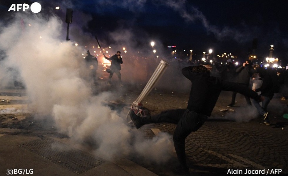 Un manifestant masqué déplace une barricade au milieu des gaz lacrymogènes, des flammes et des projectiles lors des rassemblements parisiens du 16 mars 2023.