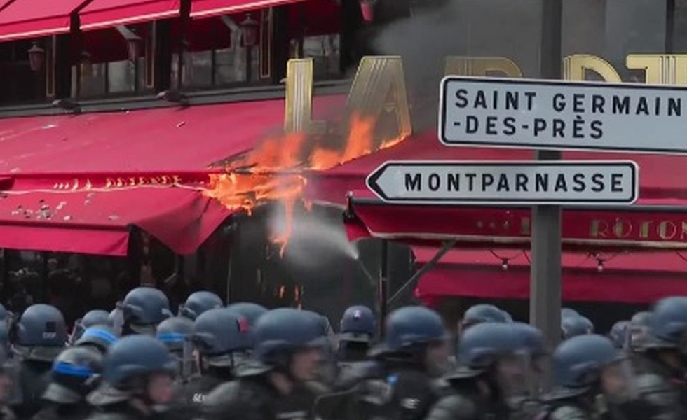 Des flammes et de la fumée s’échappent de l’auvent de la brasserie La Rotonde, derrière une ligne de policiers antiémeute, le 6 avril 2023.