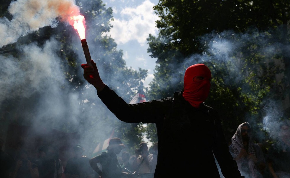 Un manifestant masqué brandit un fumigène rouge au milieu d’un nuage de fumée pendant le cortège parisien du 1er mai 2025.