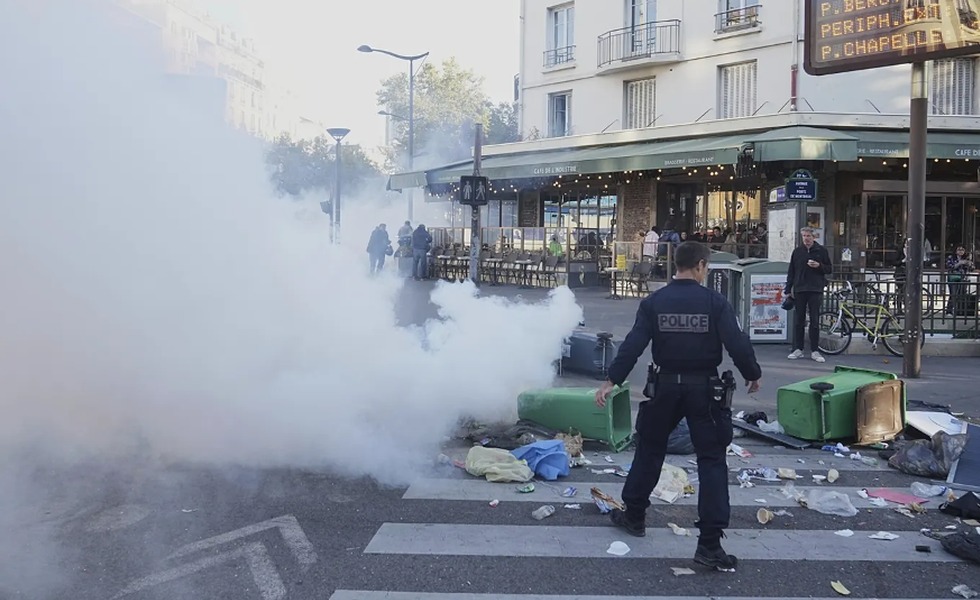 Un policier fait face à une rue parisienne encombrée de poubelles renversées et de barricades, sous un nuage de gaz lacrymogène, pendant « Bloquons tout ».