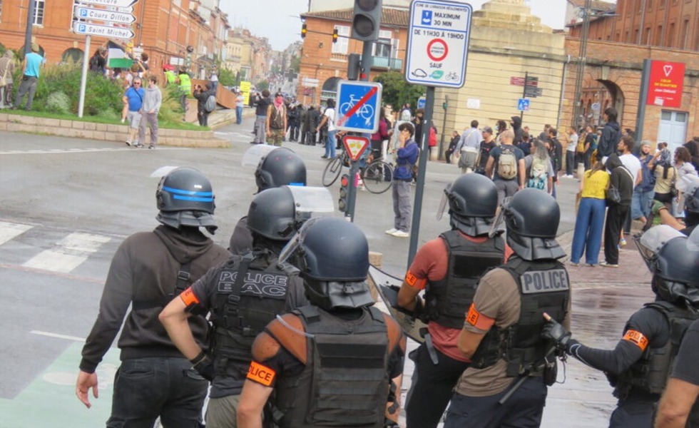 Des policiers antiémeute font face à un rassemblement dans une rue de Toulouse, alors que des manifestants et des projectiles occupent l’intersection.