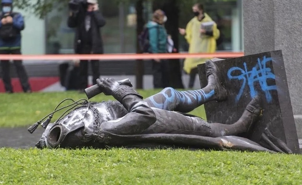 La statue décapitée de John A. Macdonald repose sur le gazon, maculée de peinture bleue, tandis que des témoins se tiennent derrière un ruban de sécurité. Photo : Graham Hughes / La Presse canadienne, publiée par Global News.