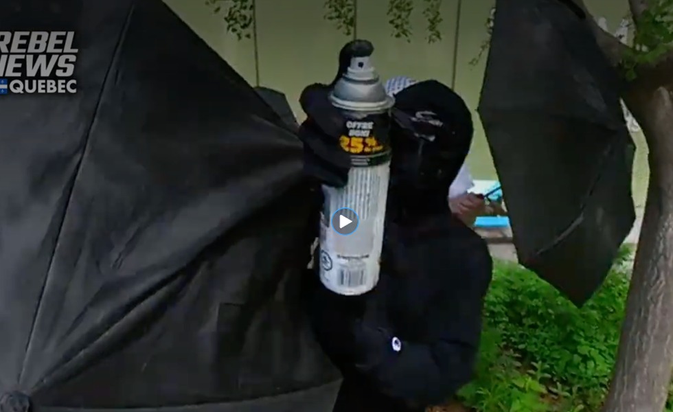 Une personne vêtue de noir, le visage dissimulé, pointe une bombe aérosol vers la caméra de l’équipe de Rebel News au campement de l’UQAM. Capture du reportage de Rebel News / YouTube.