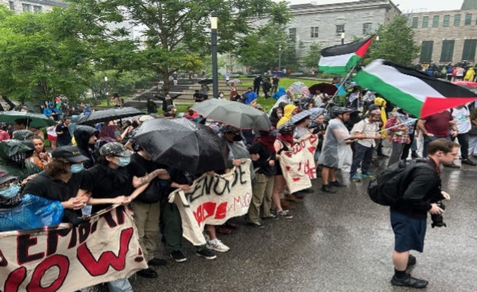 Sous la pluie, des manifestants poussent ou retiennent une barrière métallique devant le pavillon administratif de McGill; un drapeau palestinien flotte au-dessus du groupe. Photo : Giuseppe Valiante / La Presse canadienne, publiée par CityNews.