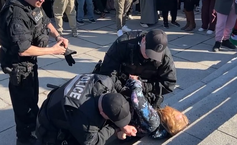 Des policiers maîtrisent et menottent Natasha Graham au sol pendant la marche du 13 avril 2025. Capture du reportage de Rebel News / YouTube.