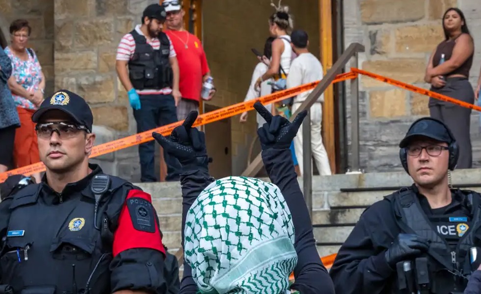 Des policiers et des participants occupent les marches et l’entrée d’une église, délimitée par du ruban orange, tandis qu’une personne portant un keffieh se tient au premier plan. Capture d’un reportage sur le concert de Sean Feucht, publiée par CityNews.