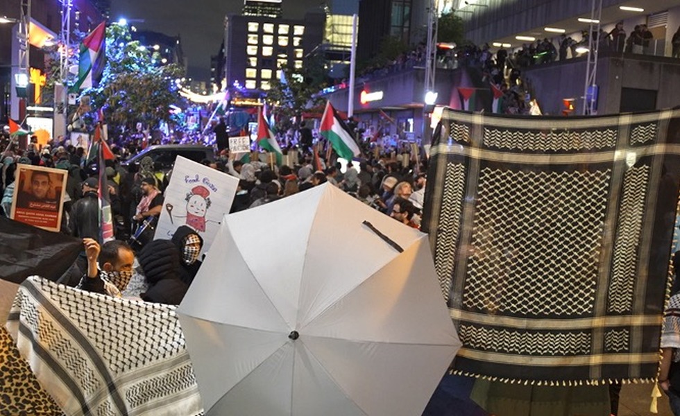 Une foule dense, munie de parapluies et de drapeaux palestiniens, se presse contre des barrières métalliques lors des incidents du 7 octobre 2025. Capture du reportage de Rebel News / YouTube.