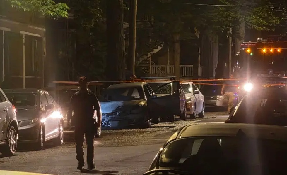 Un véhicule incendié et lourdement endommagé se trouve dans une rue résidentielle de nuit, près d’un véhicule d’urgence. Image publiée dans les reportages cités sur l’incendie de la voiture d’Alexandre Cormier-Denis.