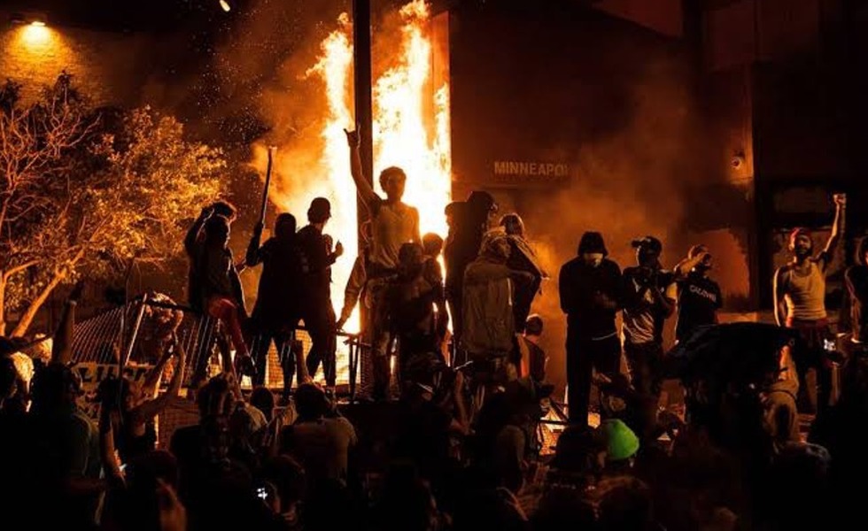 Une foule se tient devant le 3e commissariat de Minneapolis, dont la façade est entièrement embrasée dans la nuit du 28 mai 2020.
