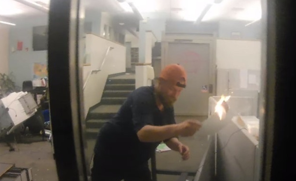 À l’intérieur du Justice Center de Portland, un homme tient un objet enflammé au milieu de bureaux renversés et d’une épaisse fumée.