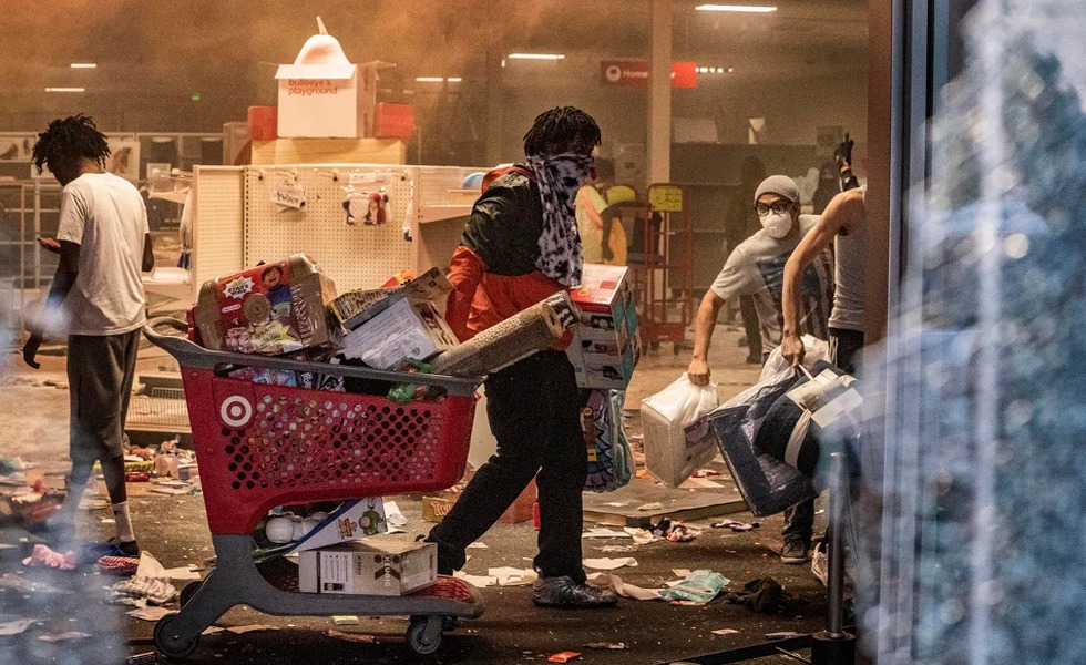 Des personnes transportent des marchandises dans un magasin Target saccagé, au milieu de débris et de fumée.