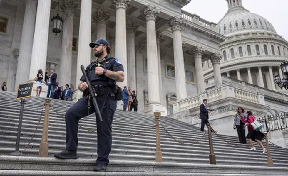 Un agent armé assure la sécurité sur les marches du Capitole des États-Unis, devant les colonnes du bâtiment.