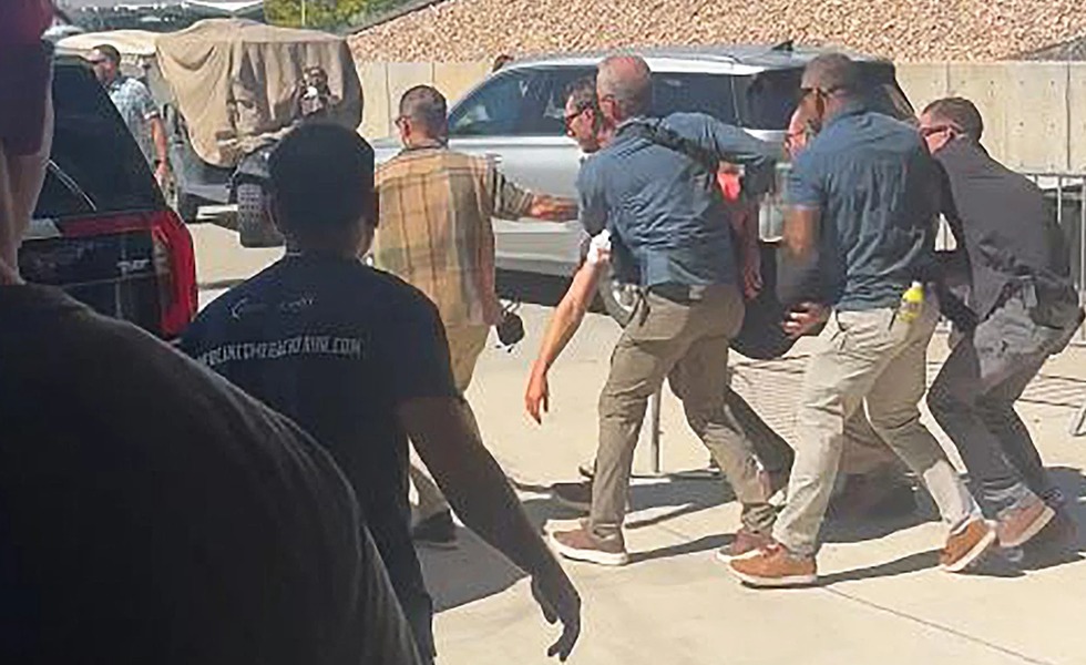 Des agents de sécurité et des secouristes transportent une personne blessée hors d’un rassemblement extérieur.
